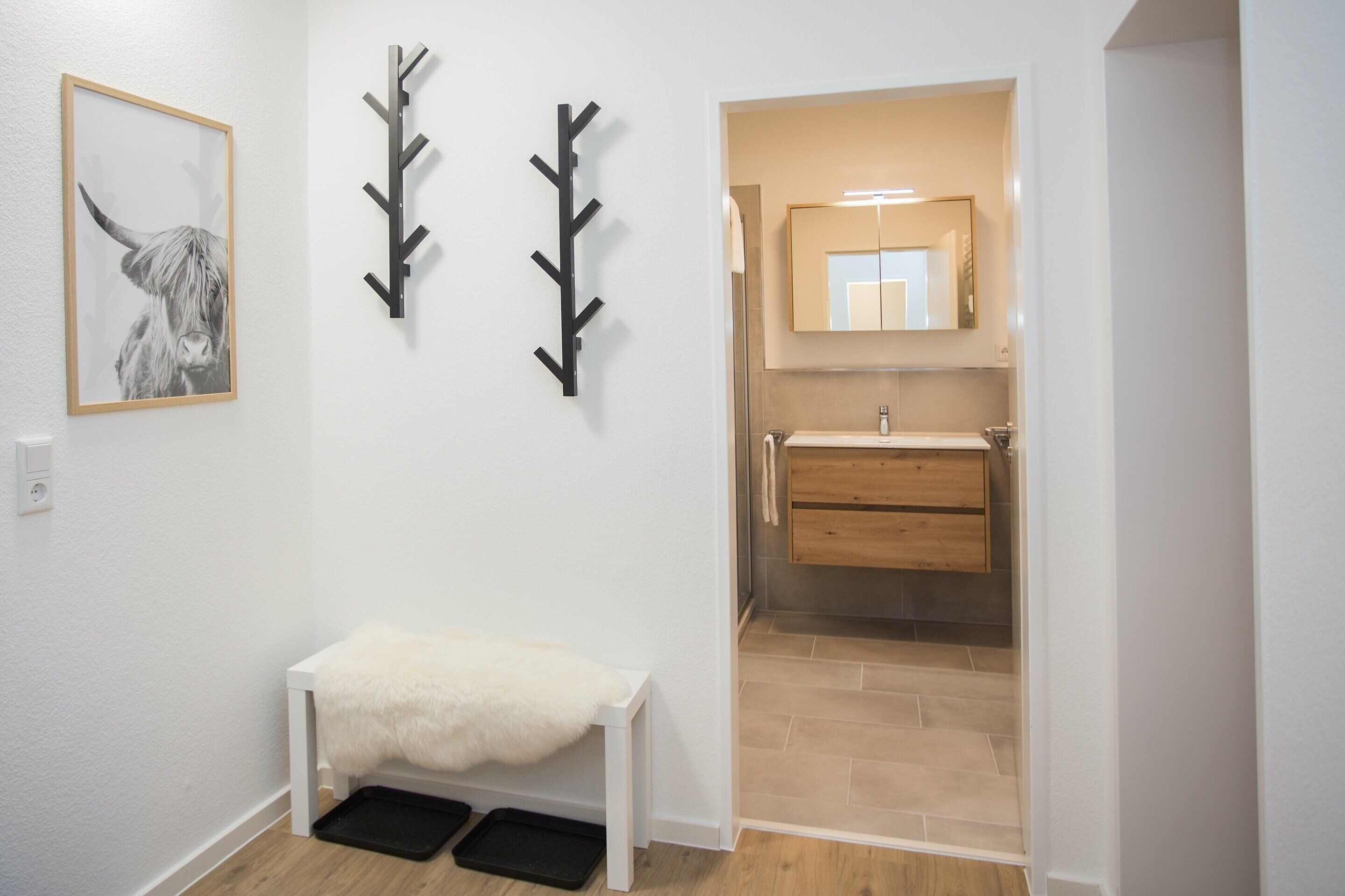 A hallway with a white bench, a black coat rack, and a framed picture of a yak.
