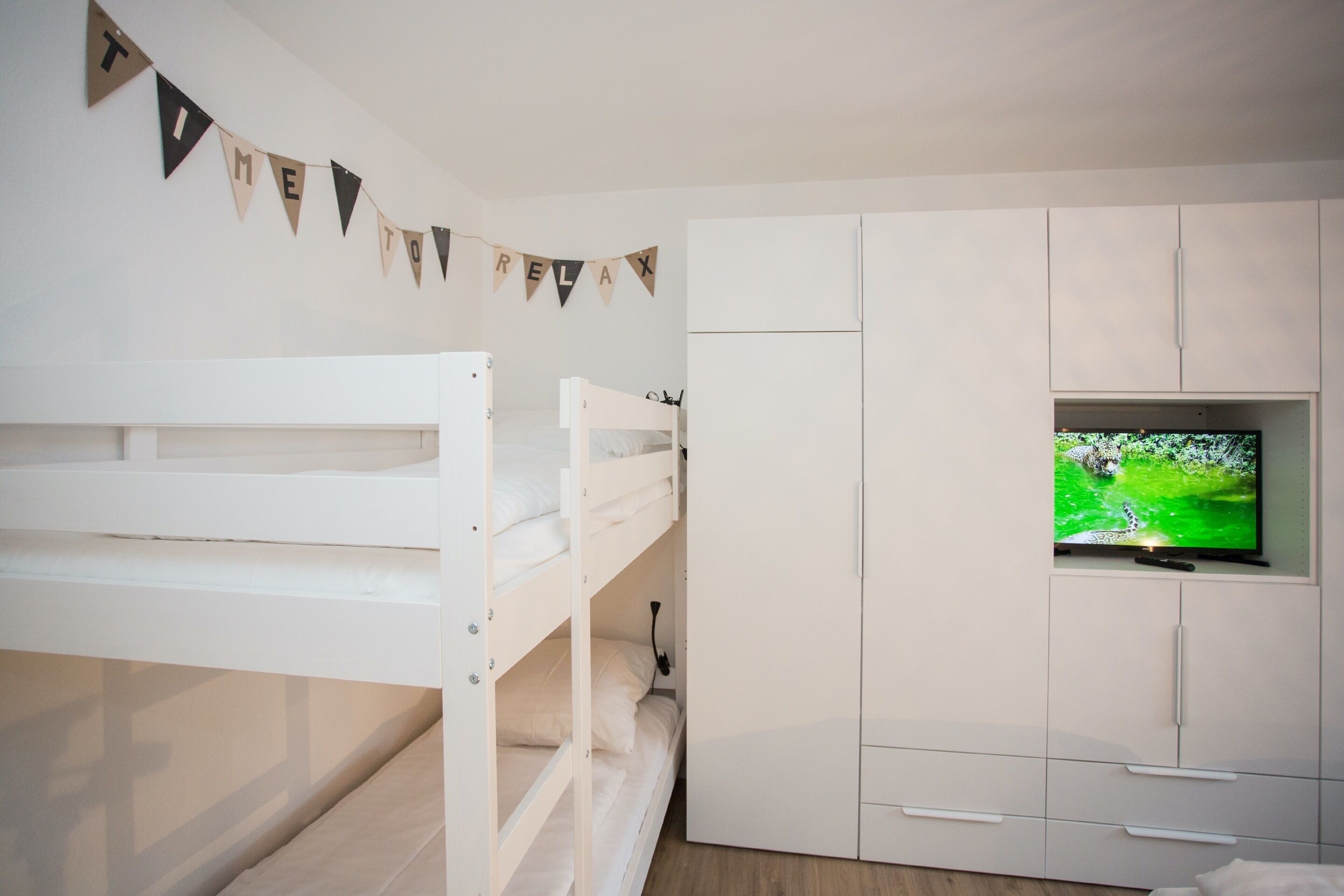 Une chambre avec un lit superposé, une télévision et une armoire.