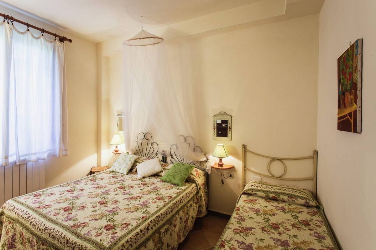 Une chambre avec deux lits simples, une table de chevet avec une lampe, un miroir et une fenêtre avec des rideaux.