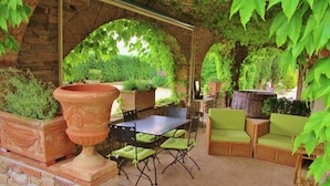 An outdoor patio with brick walls, green cushioned chairs, a table, and potted plants. - Farmhouse in Marsciano With Vineyards Olive Groves (Marsciano)