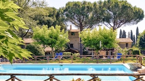 A pool area with a wooden fence, blue lounge chairs, and a stone building in the background. - Farmhouse in Marsciano With Vineyards Olive Groves (Marsciano)