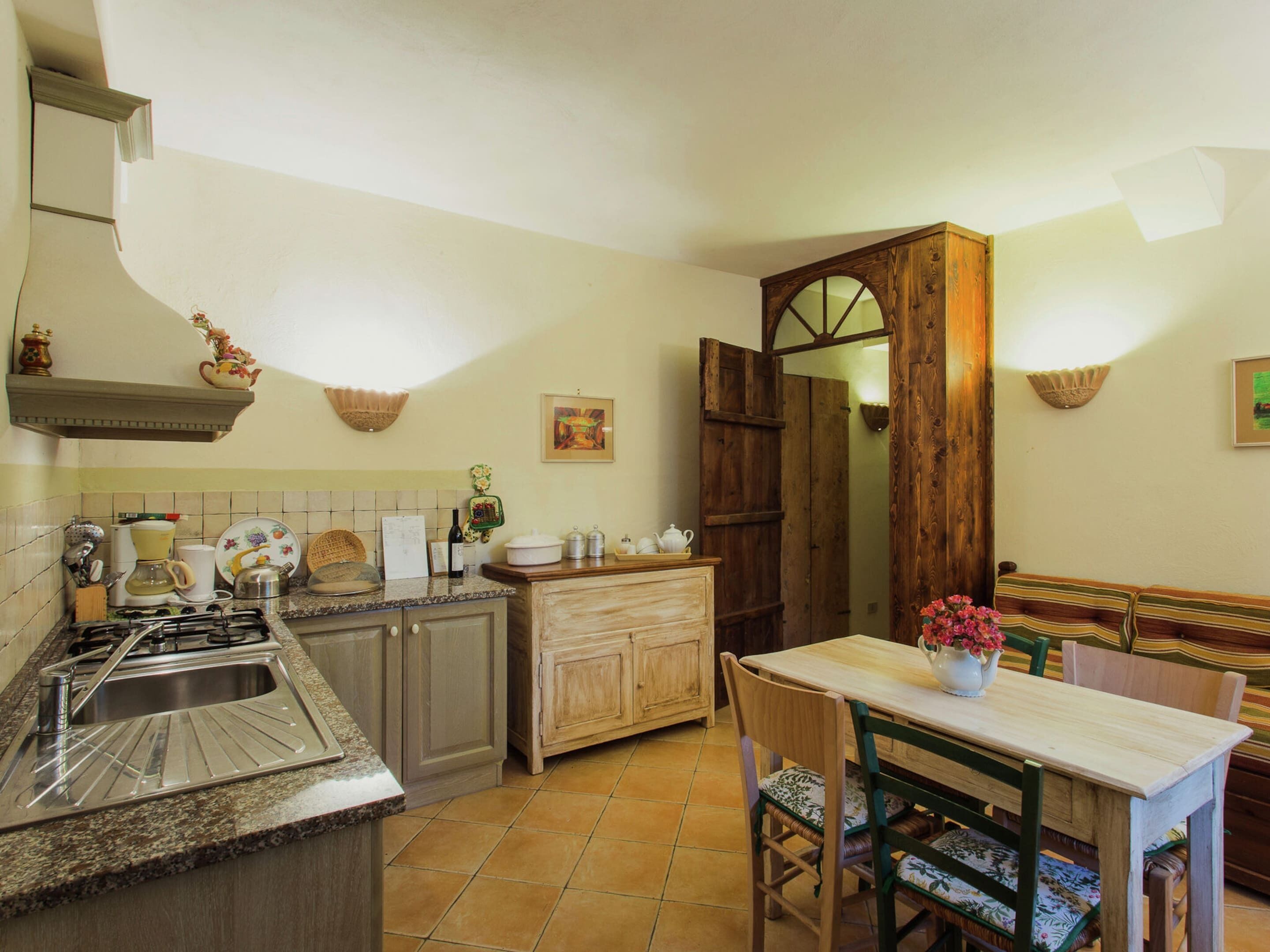 A kitchen with a stove, sink, and wooden cabinets. There is a dining table with chairs and a bench.