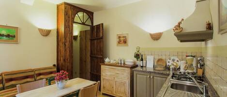 Une cuisine chaleureuse avec une table en bois, des chaises et un banc. On y trouve un évier, une cuisinière et des placards.