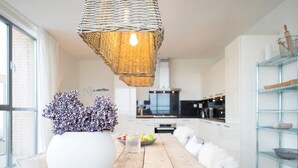 Een moderne keuken met een houten tafel, een witte vaas met paarse bloemen en een hangende rieten lamp.