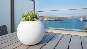 Een witte plantenbak op een balkon met uitzicht op zee en boten.