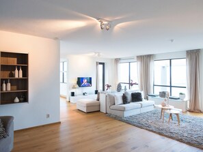 A modern living room with a sofa, a TV, a bookshelf, and a large window. - Spacious Modern Apartment in Scheveningen (The Hague)