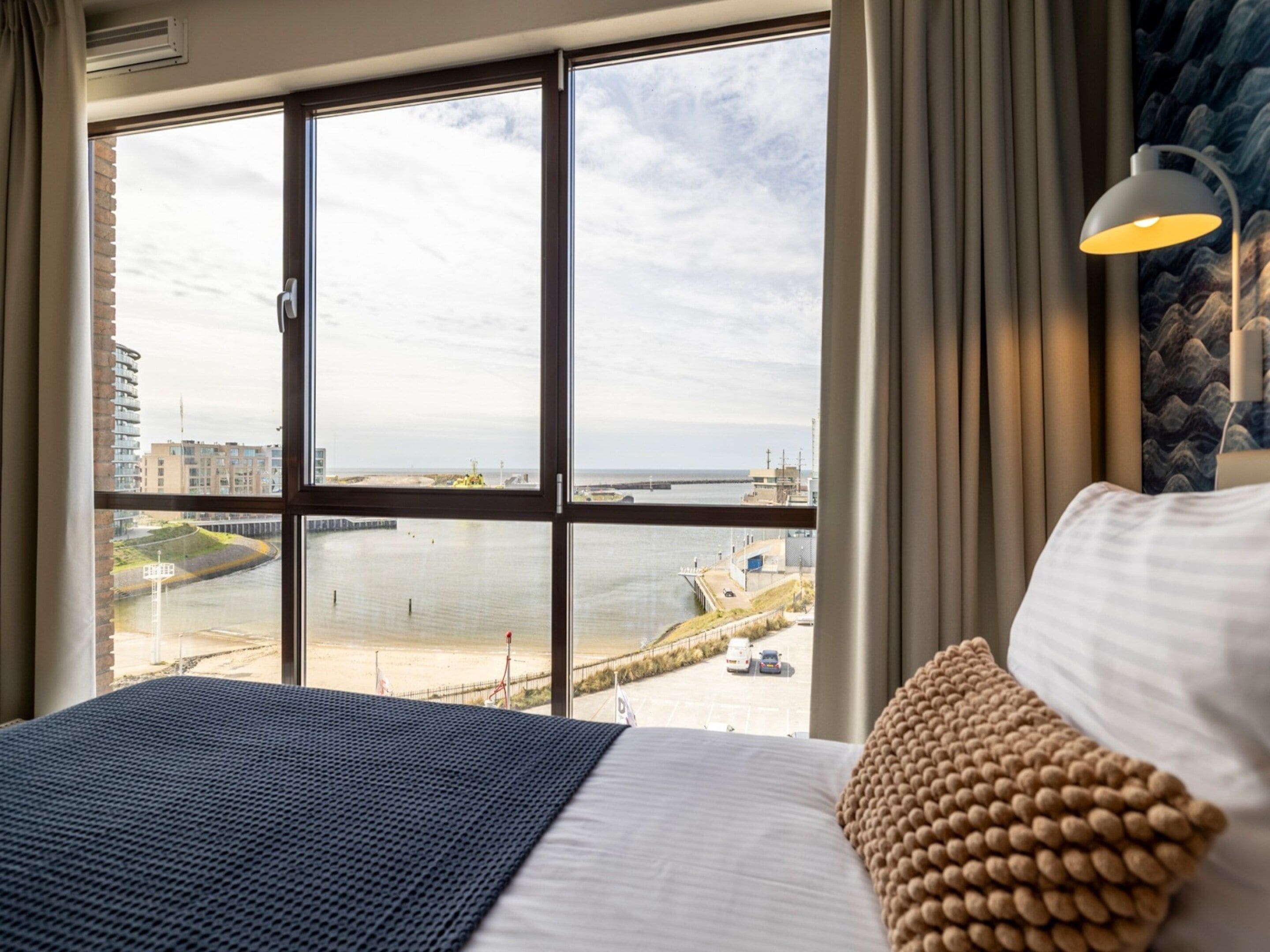 Habitación de hotel con un ventanal grande que ofrece vistas al mar y a un muelle.