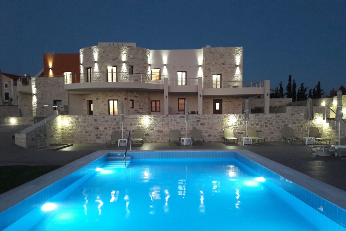 Une piscine bordée d’un mur en pierre, avec un immeuble à plusieurs étages en arrière-plan.