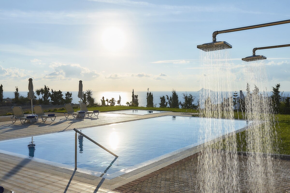 Une piscine agrémentée d’une cascade, de chaises longues et offrant une vue sur l’océan.