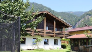 Un chalet en bois doté d’un balcon, d’une façade blanche et offrant une vue sur un paysage montagneux.