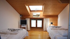 Une chambre avec deux lits, une télévision, un bureau et une fenêtre de toit.