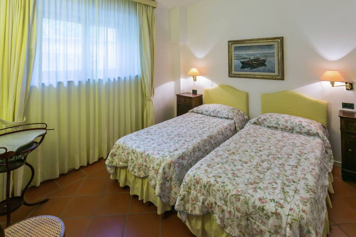 Une chambre avec deux lits, une chaise, une table et un tableau au mur.