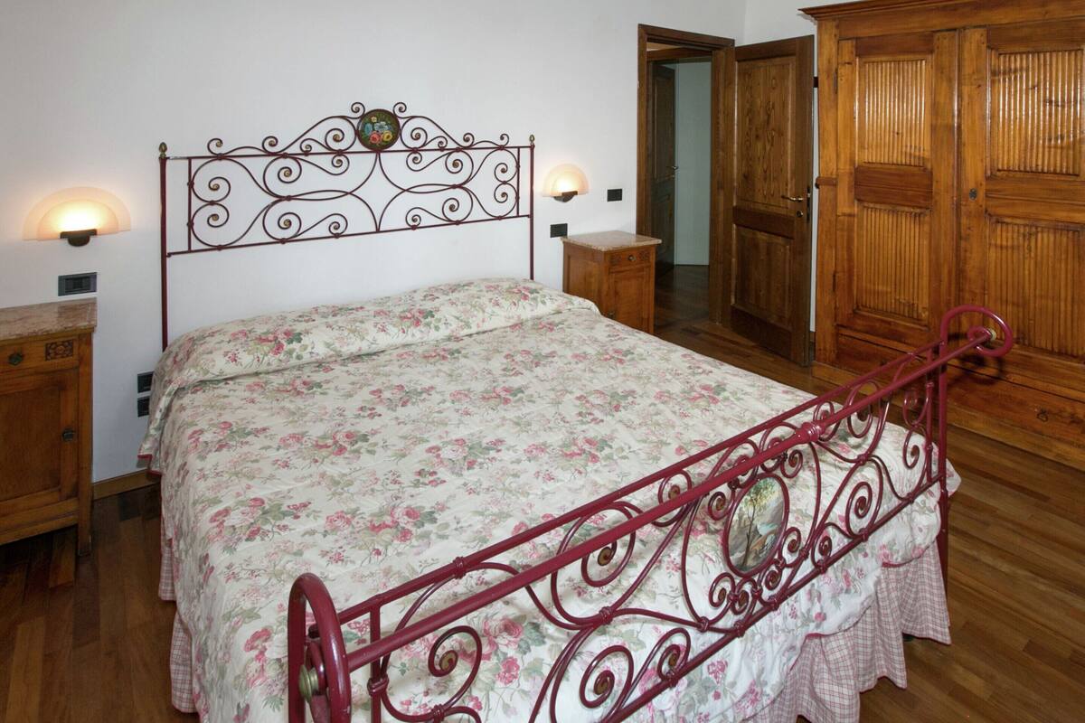 Une chambre à coucher avec un lit en métal, une couvre-lit à motifs floraux, une armoire en bois et des tables de chevet dotées de lampes fixées au mur.