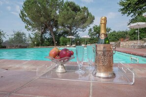Escena junto a la piscina con una botella de champán, un bol de frutas y copas sobre una bandeja transparente.