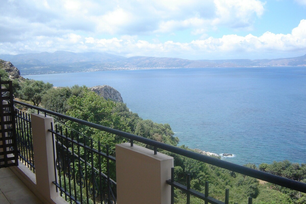 A balcony with a railing overlooking a coastal landscape with mountains and a body of water.