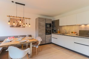 A modern kitchen with a dining area, featuring a wooden table set for four, a white chair, and a hanging light fixture. - Chalet With 2 Apartments in Kirchberg (Kirchdorf in Tirol)