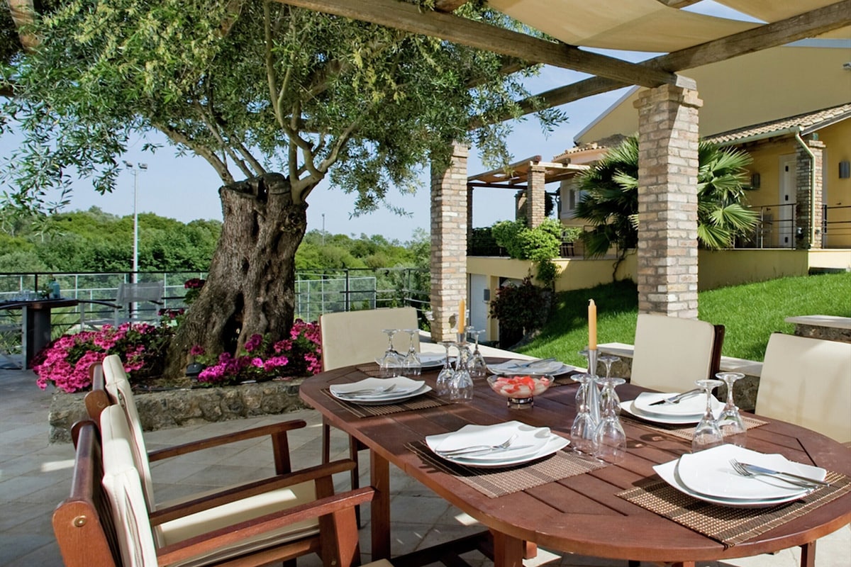 Un espace de restauration en plein air avec une table en bois, dressée pour quatre personnes, entourée de chaises, et située sous une pergola.