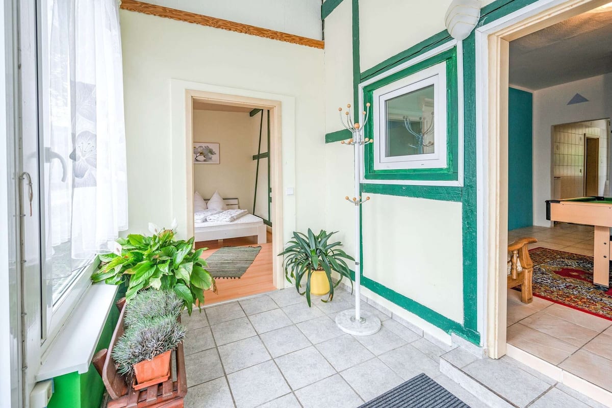 A room with a bed, a potted plant, a door leading to another room, and a window with curtains.