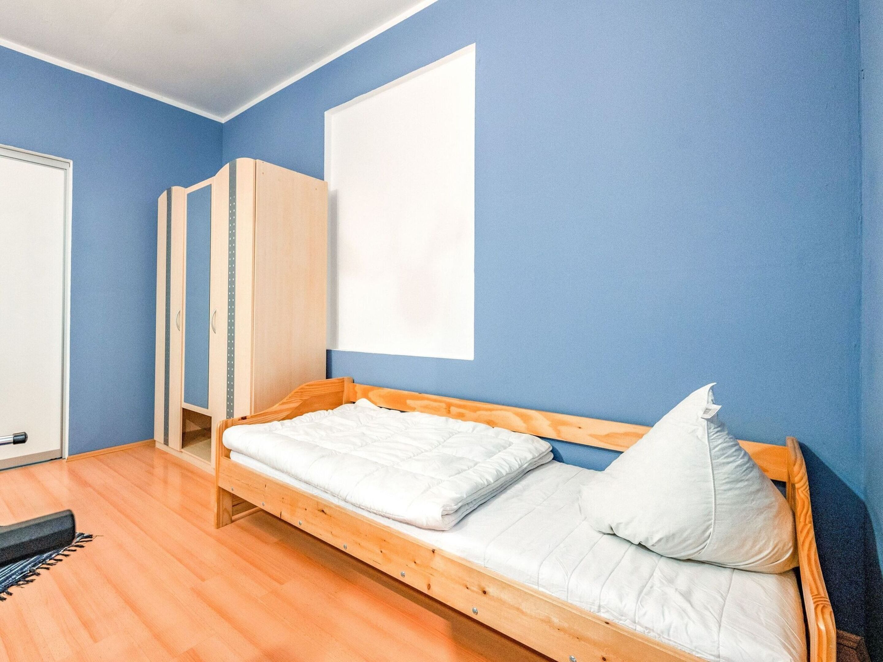 A single bed with a wooden frame and white bedding in a room with blue walls and wooden flooring.