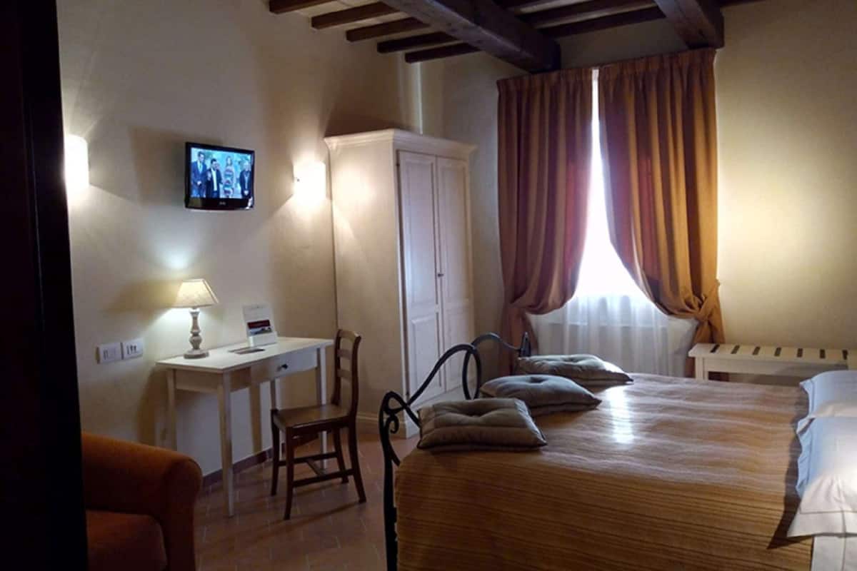 A bedroom with a wooden bed, a desk, a chair, a wardrobe, and a television on the wall.
