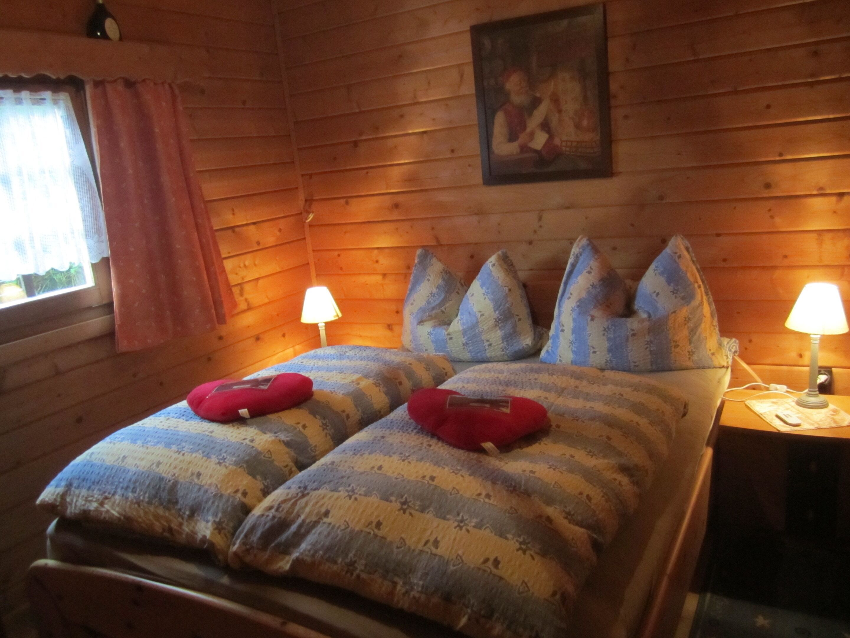 A wooden cabin bedroom with a bed, two bedside lamps, and a window with curtains.