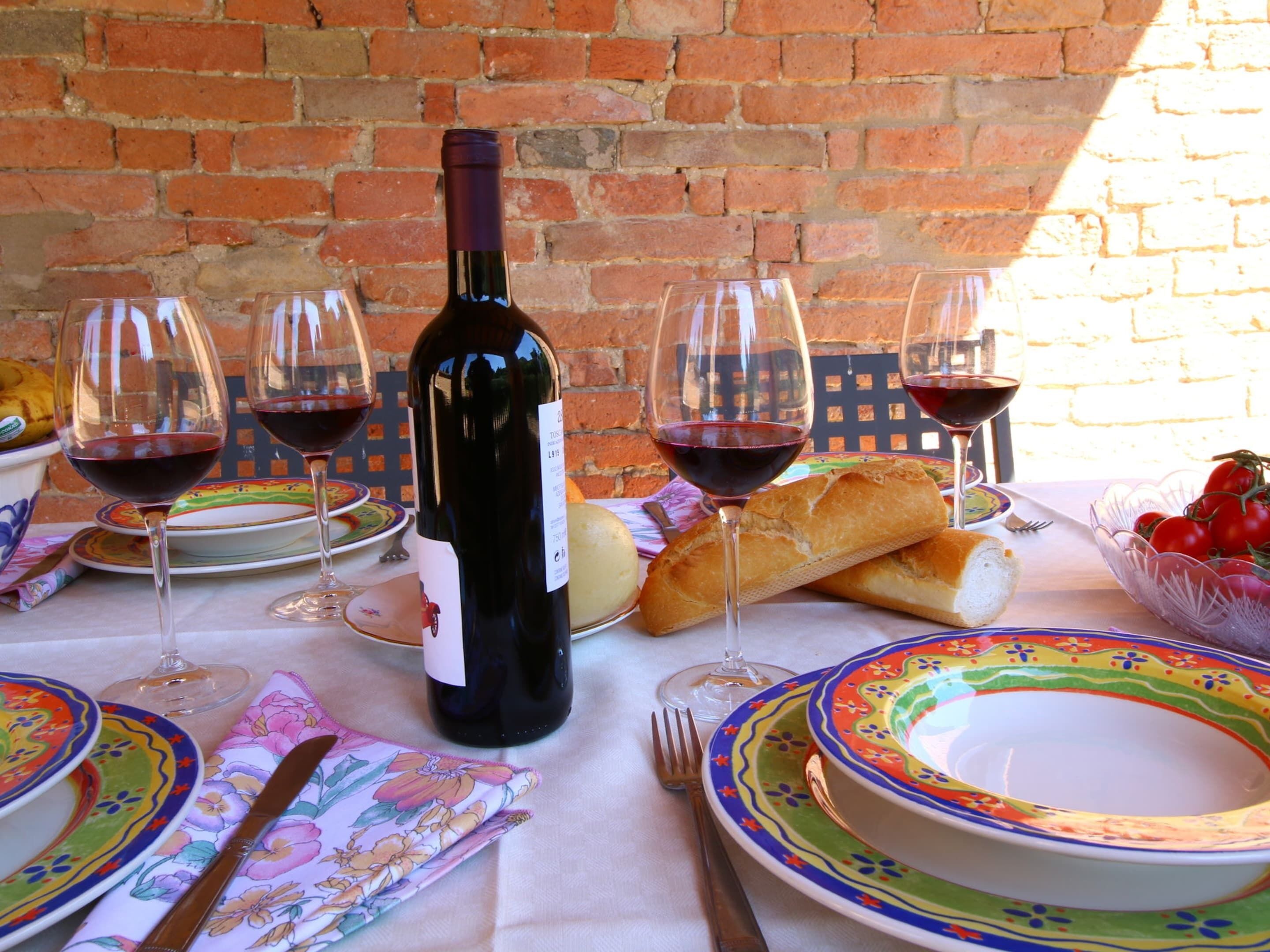 A table set with wine glasses, a bottle of wine, bread, and colorful plates.