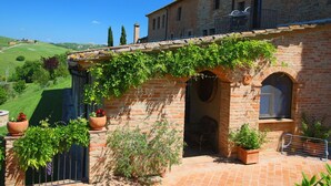 Un bâtiment rustique en briques, doté d’un balcon, de plantes en pot et offrant une vue sur un paysage vallonné.