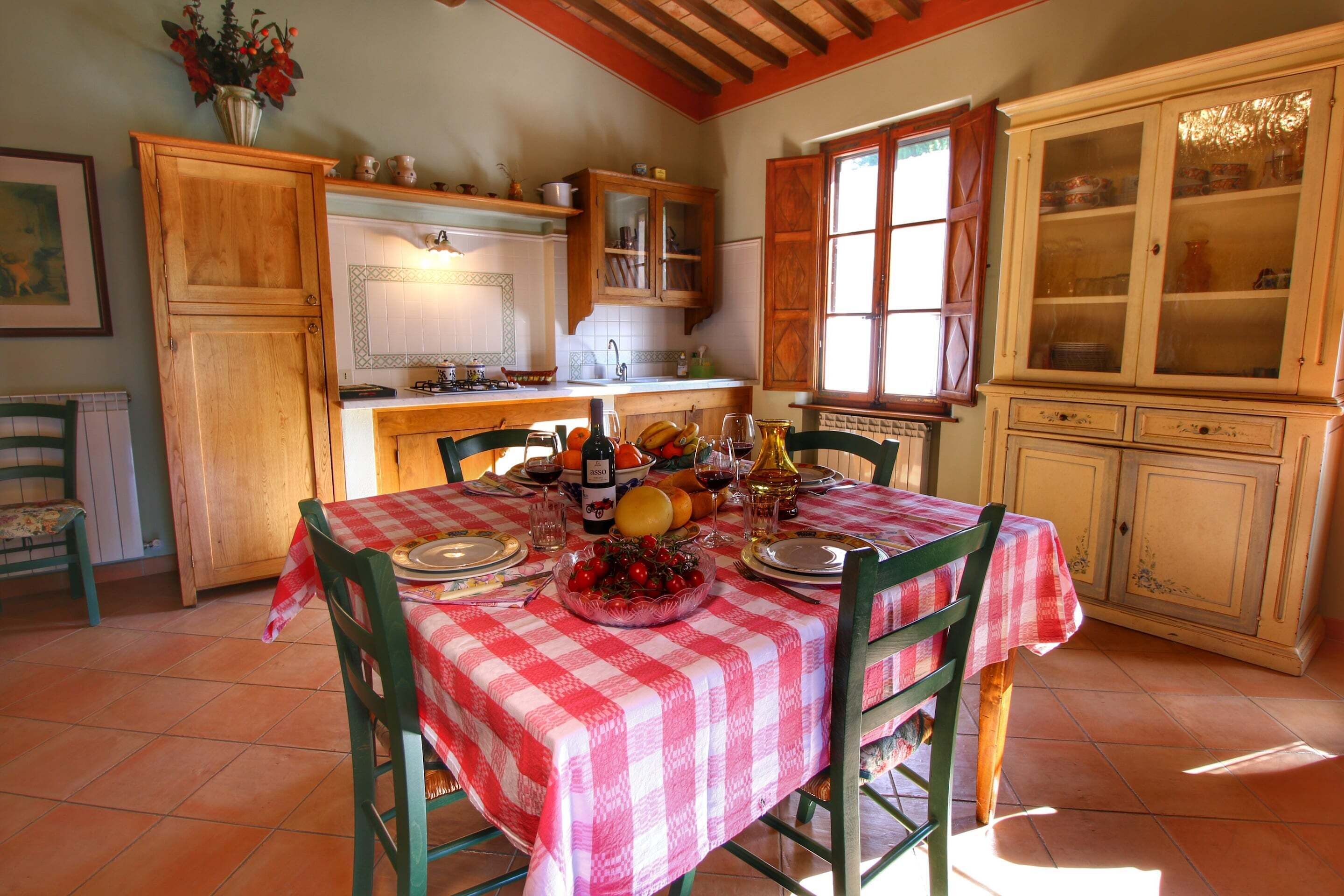 A dining area with a checkered tablecloth, wooden chairs, and a variety of food and drink items on the table.