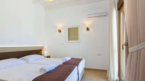 A hotel room with two beds, a bedside table with a lamp, an air conditioning unit, and a window with curtains. - Splendid Villa in Achlades With Private Pool Near Bali (Mylopotamos)
