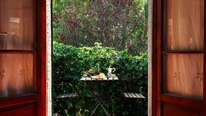A wooden door with glass panels leading to a patio with a table set for two, surrounded by lush greenery. - Rustic Farmhouse in Cortona With Swimming Pool (Cortona)
