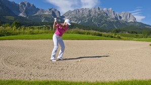 Una persona jugando golf en un campo con montañas al fondo.