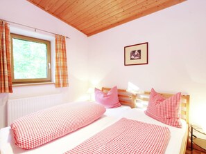 A bedroom with two beds, plaid curtains, a framed picture on the wall, and a window with a view of greenery. - Chalet in Niederndorf Near Kufstein With Balcony (Niederndorferberg)