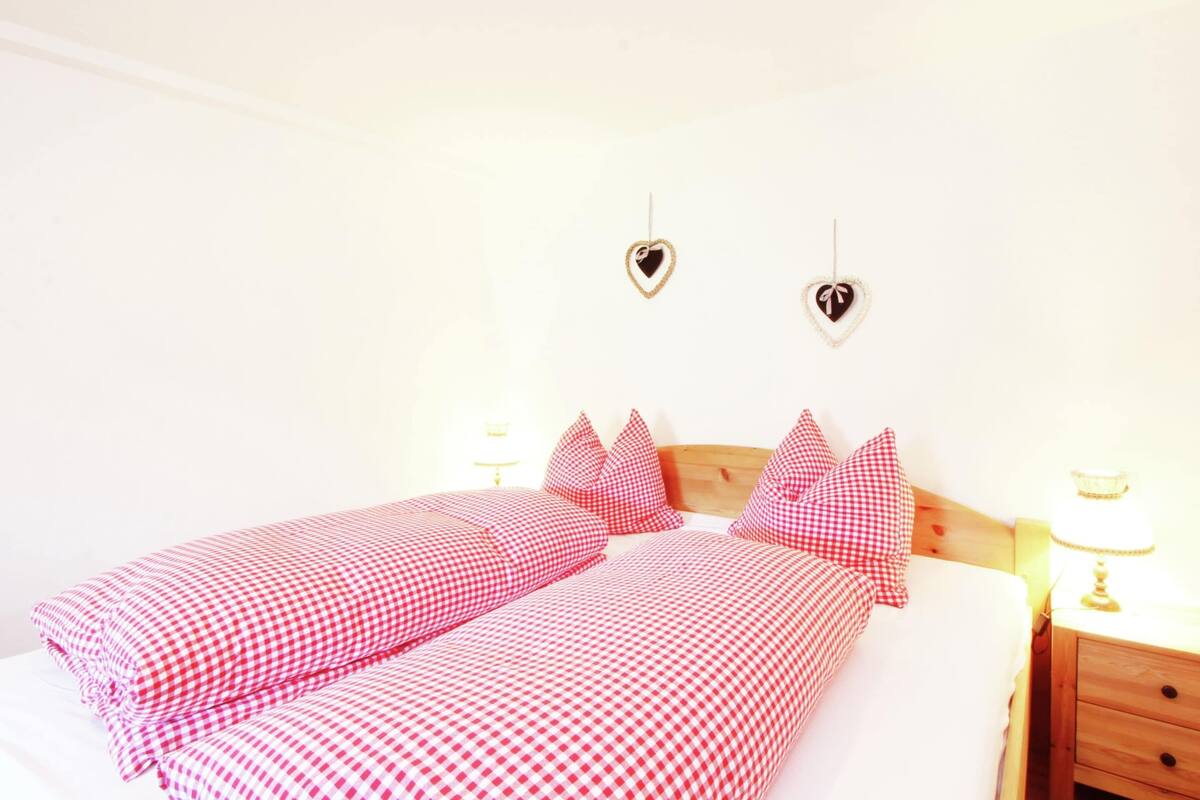 A bed with checkered bedding, two heart-shaped wall decorations, and bedside lamps.