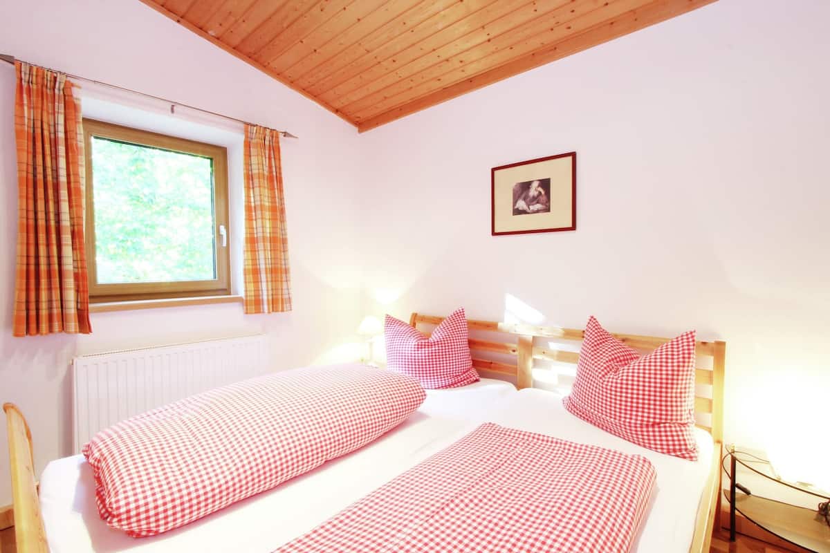 A bedroom with two beds, plaid curtains, a framed picture, and a wooden ceiling.
