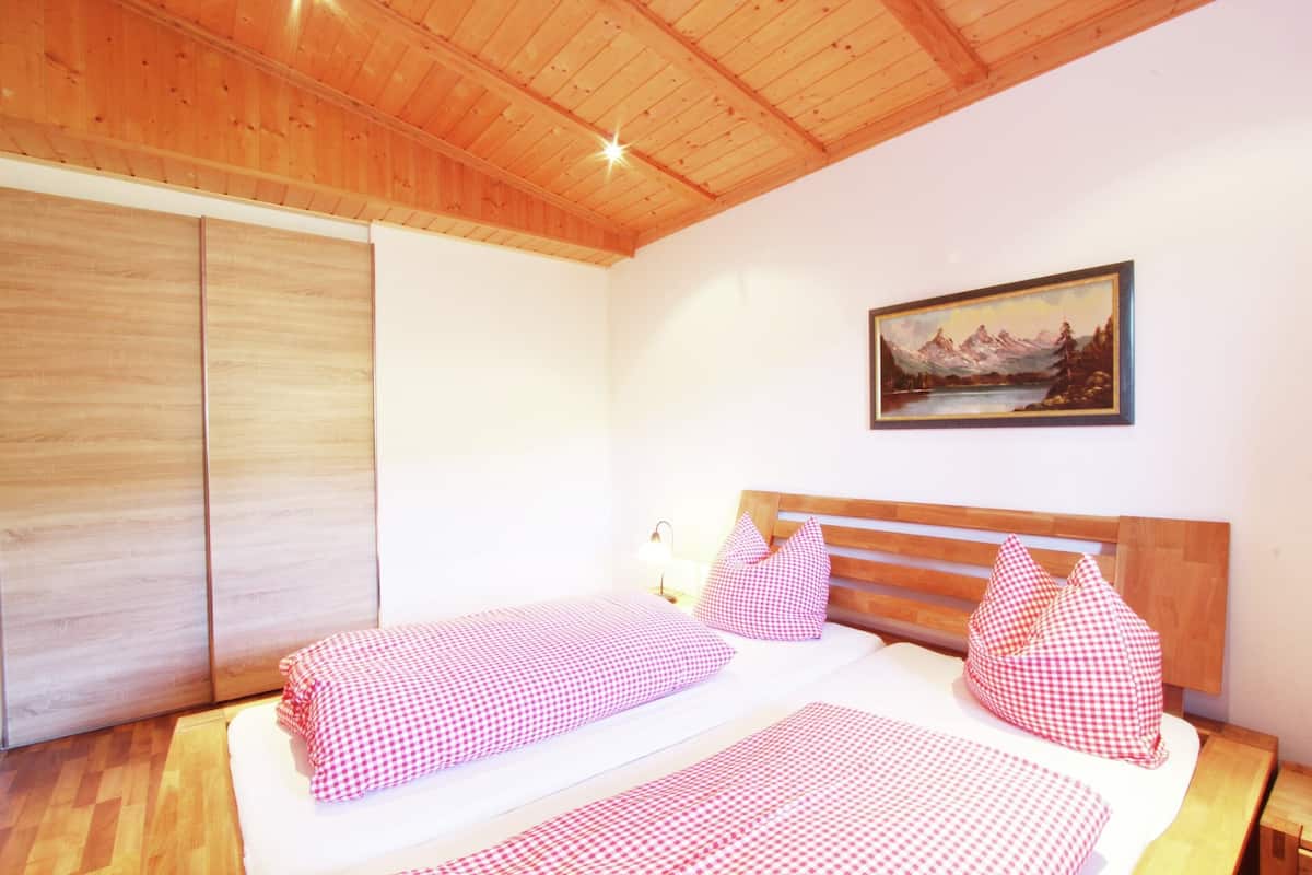 A bedroom with a wooden ceiling, a bed with checkered bedding, a nightstand, and a painting on the wall.
