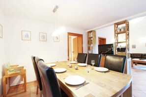 A dining area with a wooden table set for four, surrounded by black leather chairs. There are framed pictures on the wall, a wooden bookshelf, and a television in the background. - Chalet in Niederndorf Near Kufstein With Balcony (Niederndorferberg)
