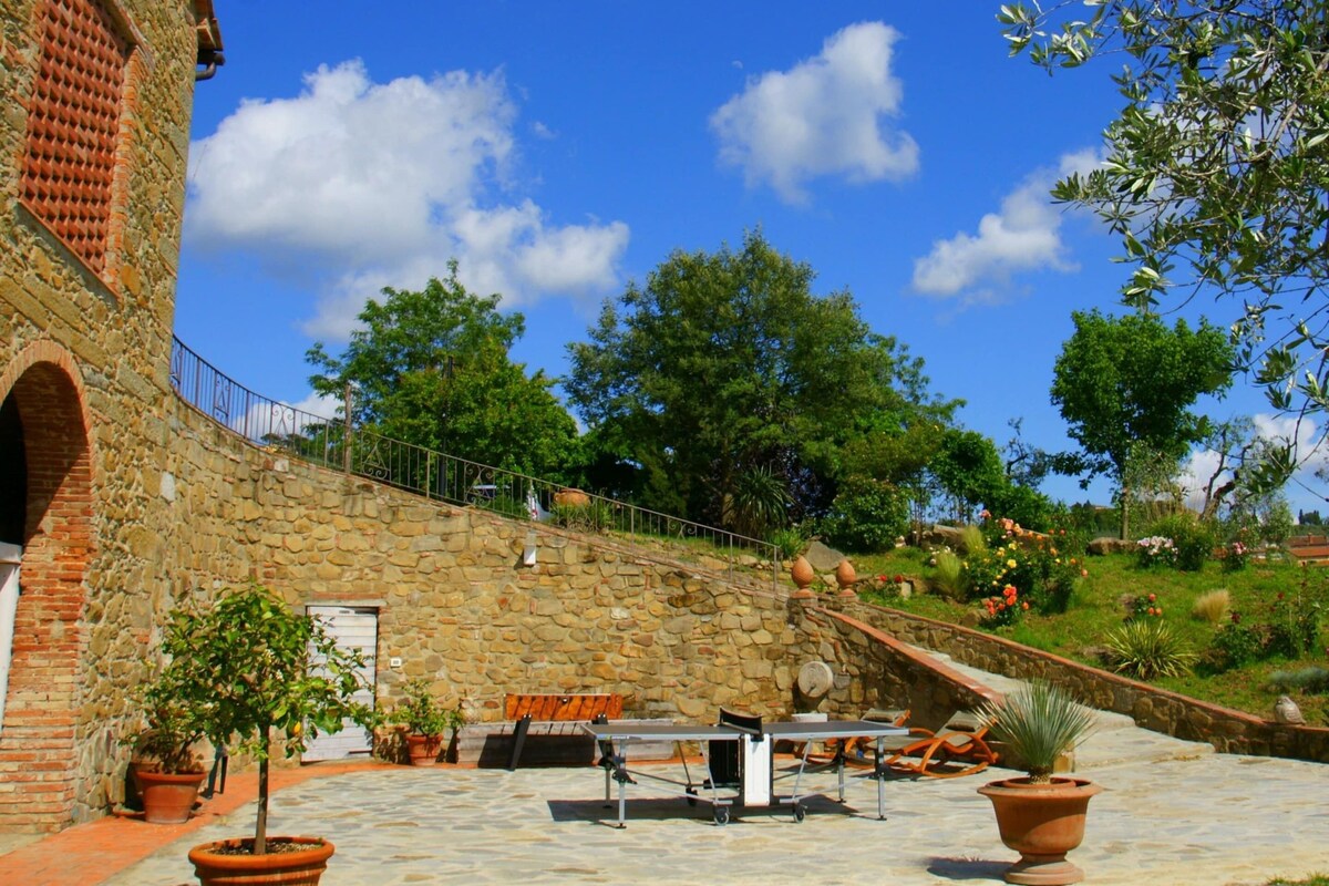 A courtyard with stone walls, a table, chairs, and potted plants.