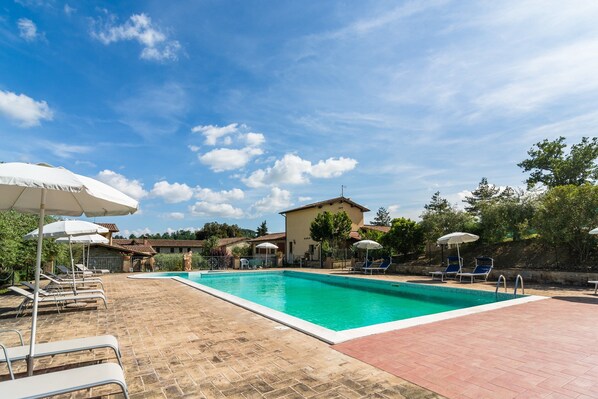 A swimming pool with lounge chairs and umbrellas, a tiled deck, and a building in the background. - Farmhouse in Perugia With Swimming Pool (Perugia)
