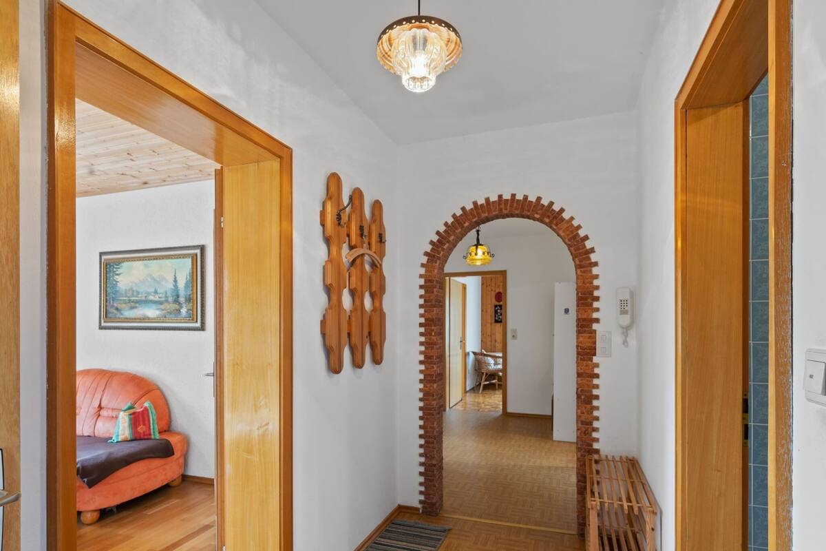 A hallway with wooden flooring, a red sofa, a wooden wall decoration, and a brick archway leading to another room.