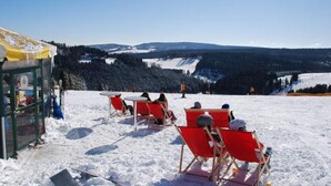 A snow-covered outdoor seating area with red chairs and tables, overlooking a snowy landscape and forested hills. - Chic Apartment in Niedersfeld Close to Hillebachsee (Winterberg)