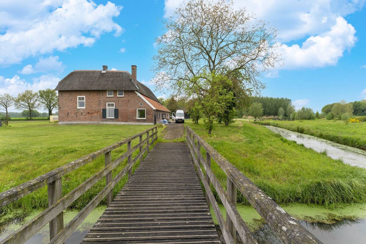 A wooden bridge leading to a brick building with a thatched roof.