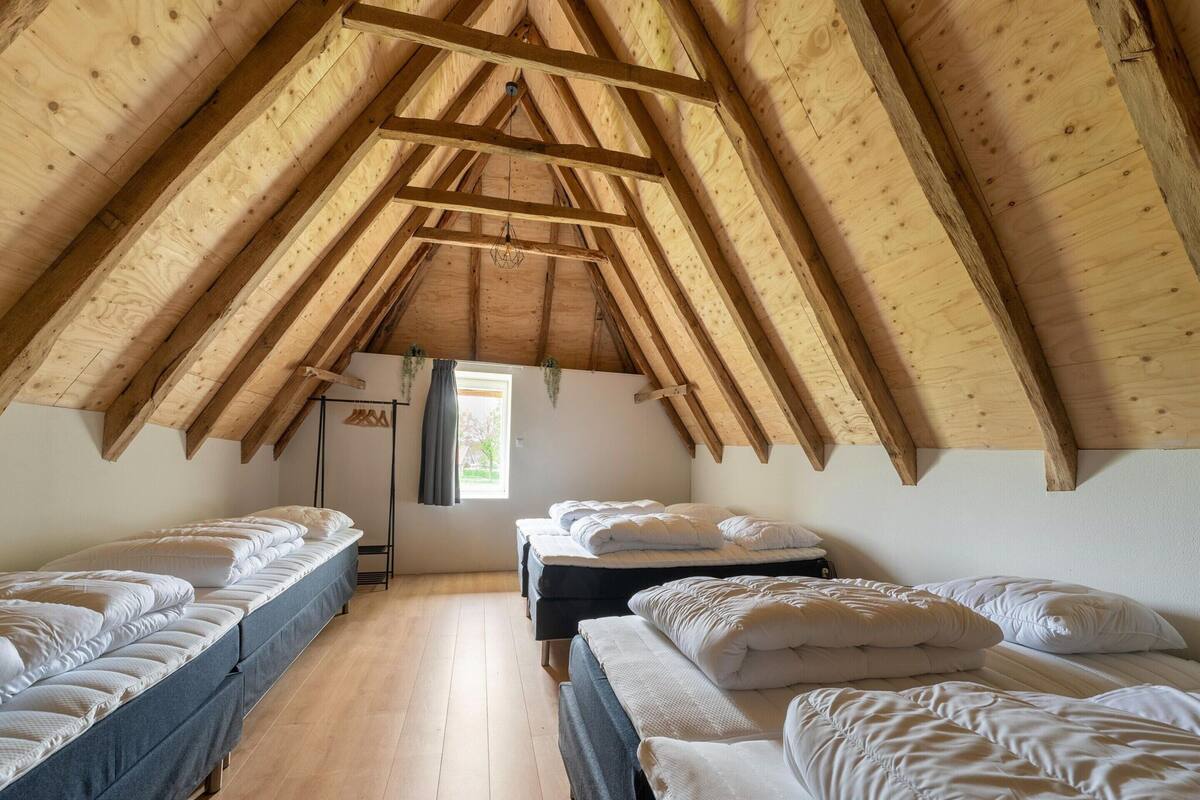 A dormitory room with wooden beams, bunk beds, a window with curtains, and a small plant.
