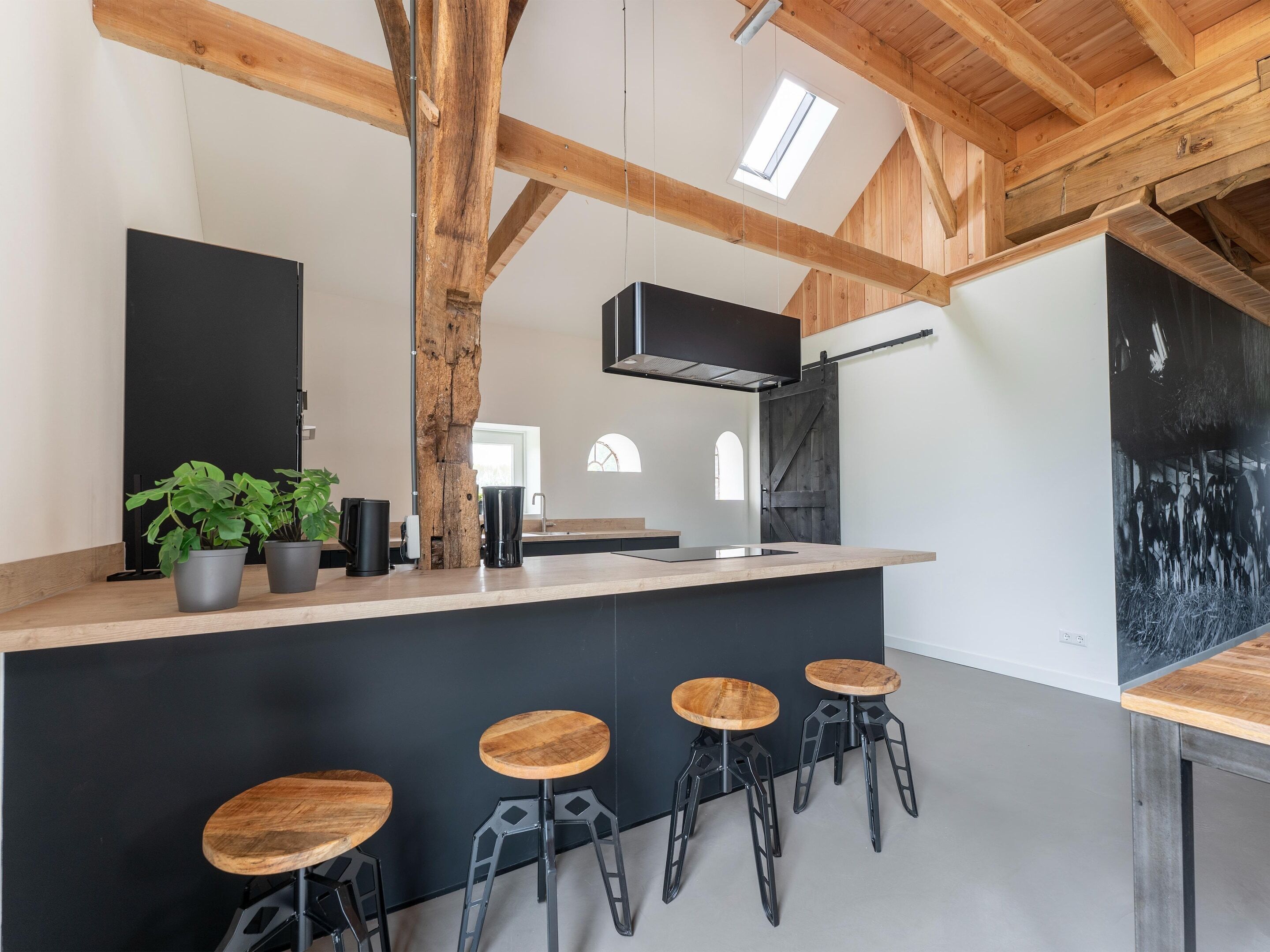 A modern kitchen with a wooden ceiling, a black countertop, and bar stools.