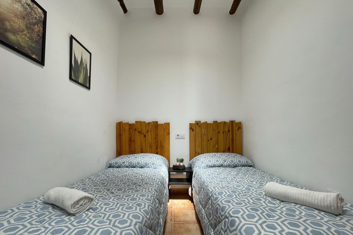 A small, clean room with two beds, wooden headboards, and a tiled floor.