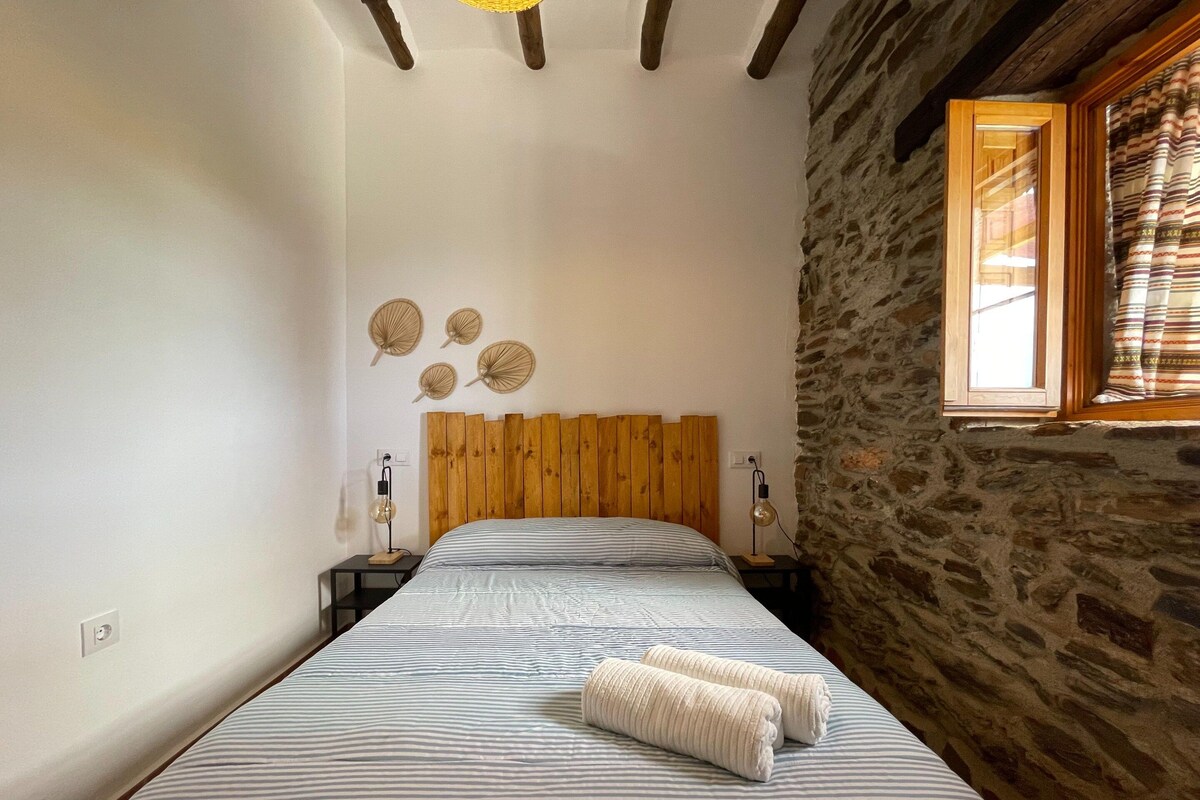 A bedroom with a wooden headboard, a bed with striped bedding, two bedside lamps, and a stone wall.