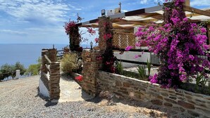En bygning i sten med udsigt over havet, med en stentrappe og blomstrende planter.