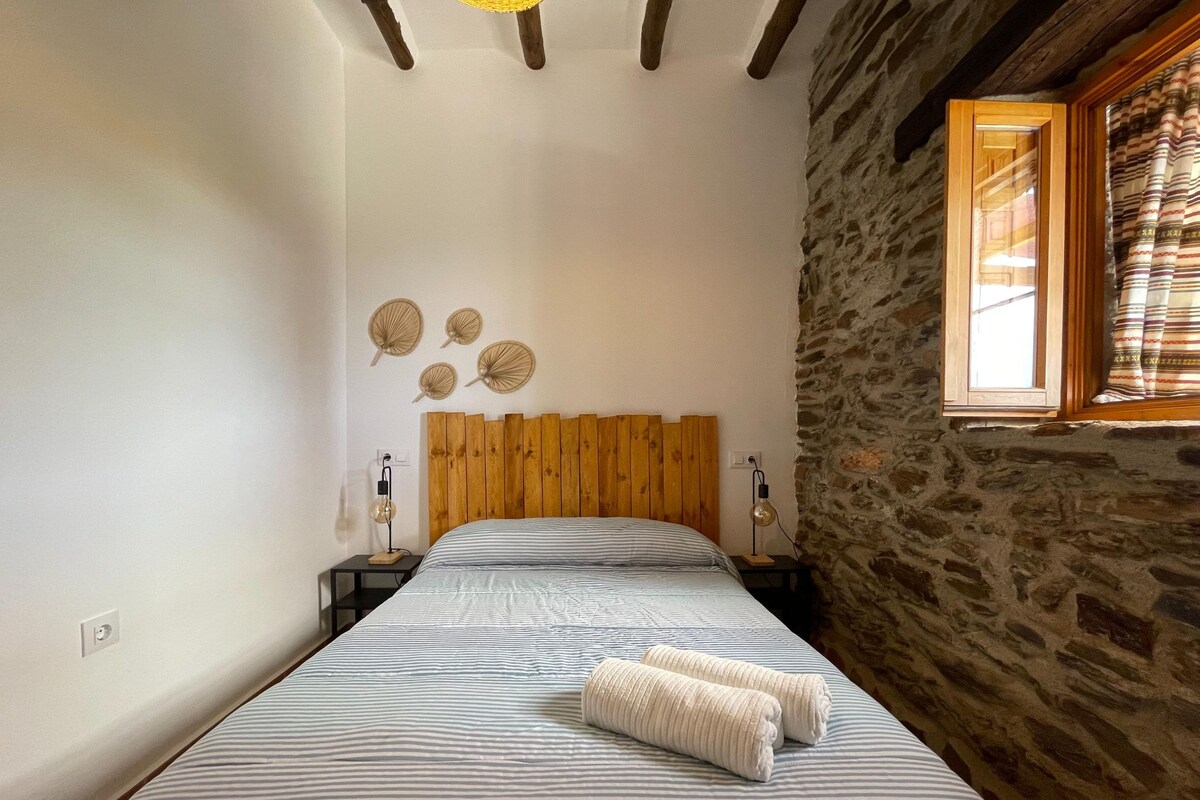 A bedroom with a wooden headboard, a bed with striped bedding, two bedside lamps, and a stone wall.