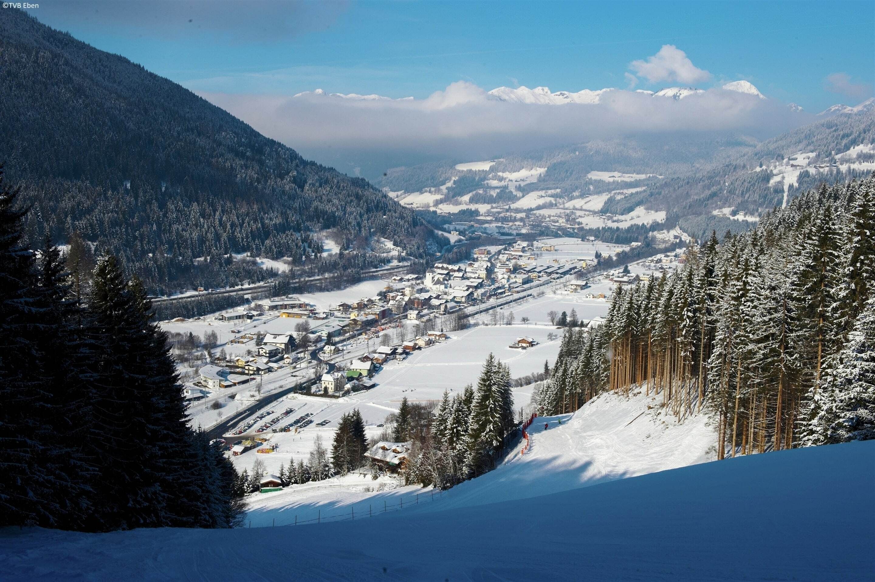 Een besneeuwde bergstad met een piste, gebouwen en een dicht bos.