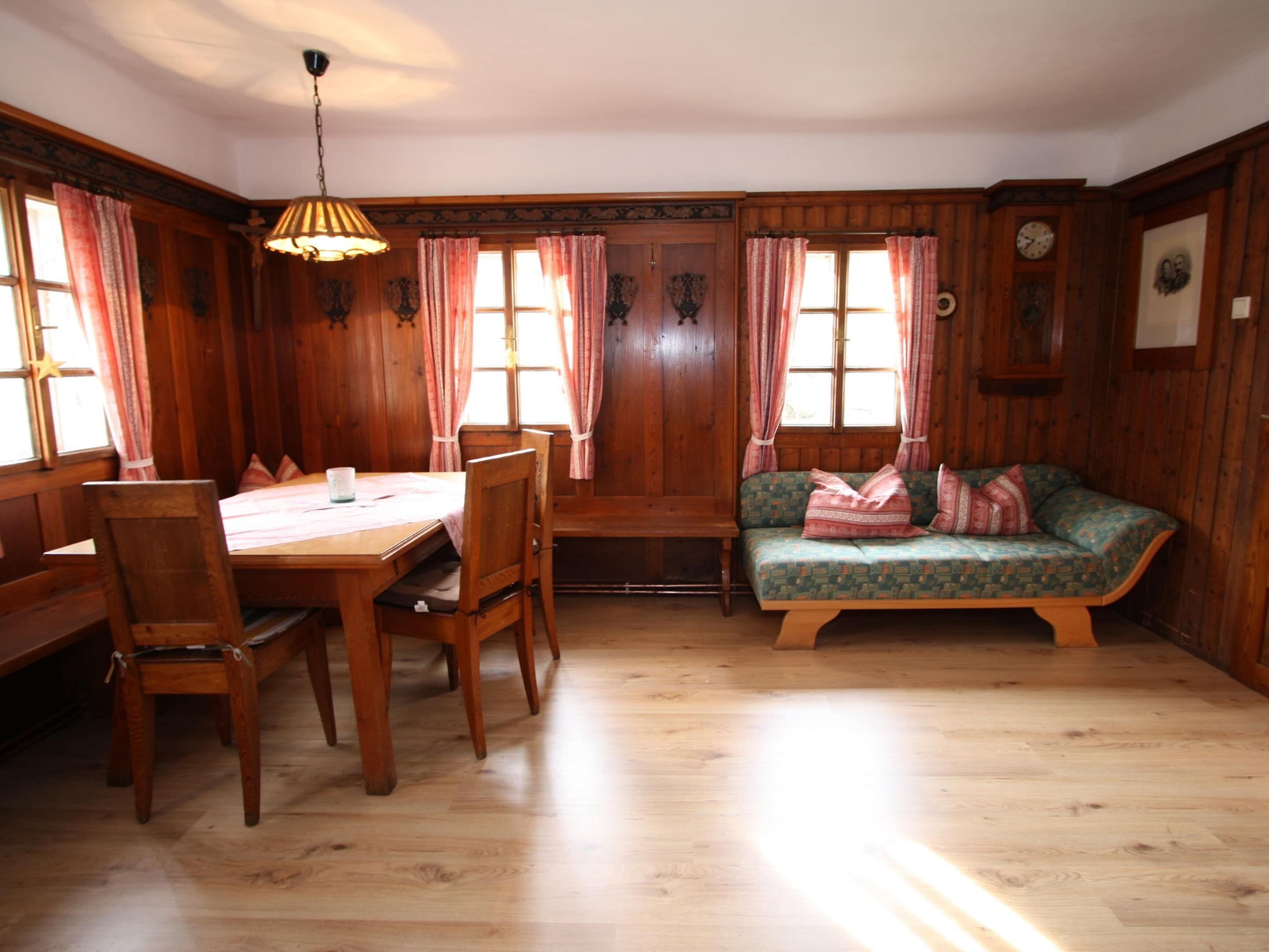 A wooden-paneled room with a dining table, chairs, and a sofa.