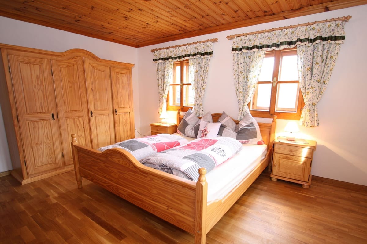A wooden-framed bed with a quilt, two bedside tables with lamps, and a wooden wardrobe.